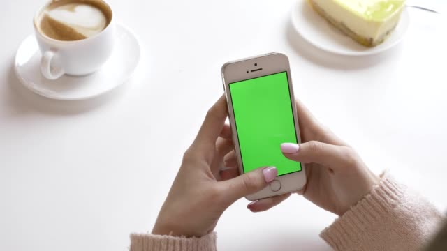 Beautiful-female-hands-using-a-smartphone-in-a-cafe,-green-screen-concept.-60-fps