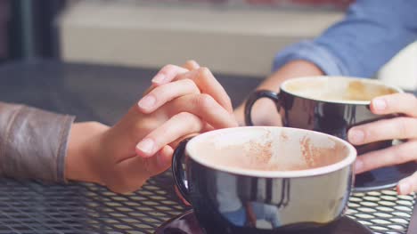 Close-up-of-a-couple-holding-hands-across-the-table-on-a-coffee-date