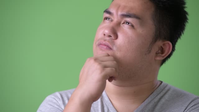 Young-handsome-overweight-Asian-man-against-green-background
