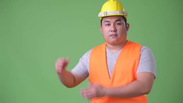 Young-handsome-overweight-Asian-man-construction-worker-against-green-background