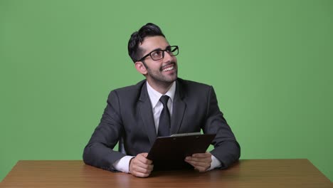 Young-handsome-bearded-Persian-businessman-against-green-background