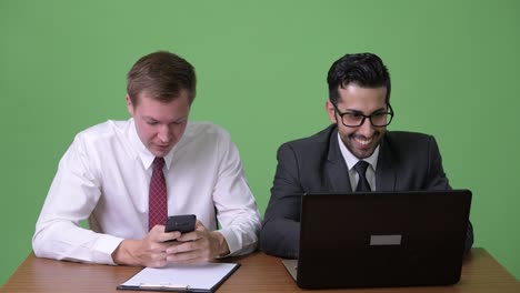 Two-young-multi-ethnic-businessmen-working-together-against-green-background