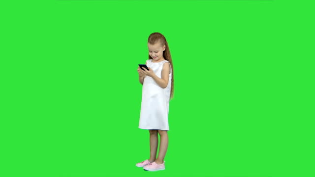 Cute-little-girl-smiling-and-uses-a-mobile-phone-on-a-Green-Screen,-Chroma-Key