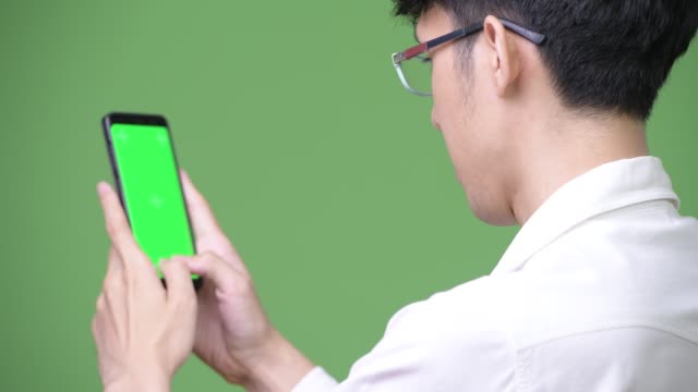 Young-Asian-businessman-using-phone-while-showing-copy-space