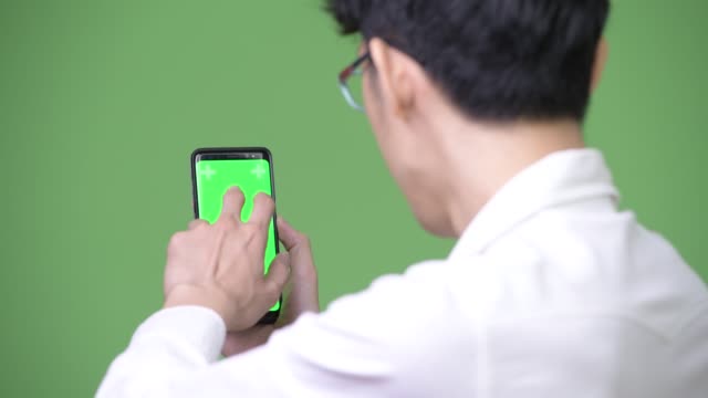 Young-Asian-businessman-using-phone-while-showing-copy-space