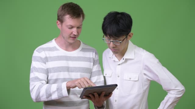 Dos-felices-empresarios-multiétnicos-joven-mostrando-tableta-digital-y-dar-pulgares-para-arriba