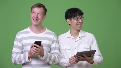 Zwei-glückliche-multiethnischen-Jungunternehmer-mit-Telefon-und-digital-Tablette-für-social-Media-Konzept