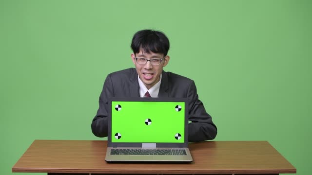 Glücklich-asiatischen-Jungunternehmer-Gefühl-aufgeregt-beim-sprechen-und-zeigen,-Laptop,-Kamera