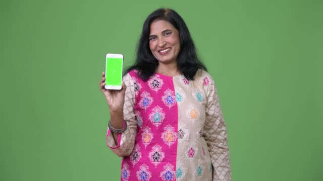 Reife-glücklich-schöne-indische-Frau-lächelnd-beim-Telefon-zeigen
