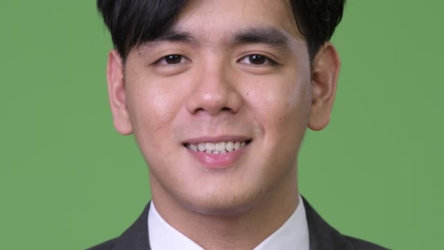 Happy-young-handsome-Asian-businessman-smiling-against-green-background