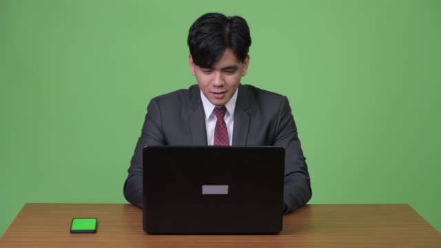 Joven-empresario-asiático-guapo-trabajando-con-ordenador-portátil-contra-el-fondo-verde