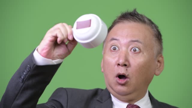 Reife-japanischer-Geschäftsmann-halten-Kaffeetasse-auf-den-Kopf-gestellt