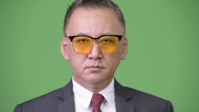 Reife-japanischer-Geschäftsmann-mit-Sonnenbrille-vor-grünem-Hintergrund