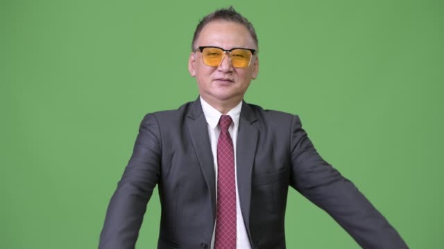 Reife-japanischer-Geschäftsmann-mit-Sonnenbrille-vor-grünem-Hintergrund