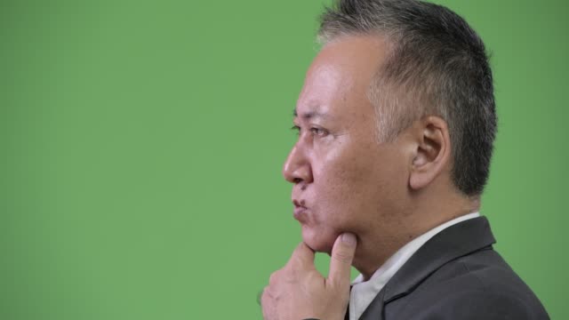 Profile-view-of-mature-Japanese-businessman-thinking-against-green-background