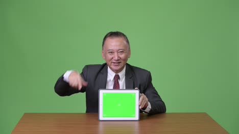 Reife-japanischer-Geschäftsmann-zeigt-digital-Tablette