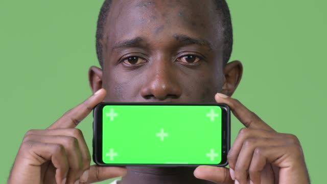 Young-African-man-showing-phone-against-green-background