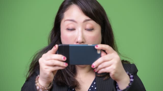 Reife-schöne-asiatische-geschäftsfrau-mit-Telefon-und-suchen-schockiert
