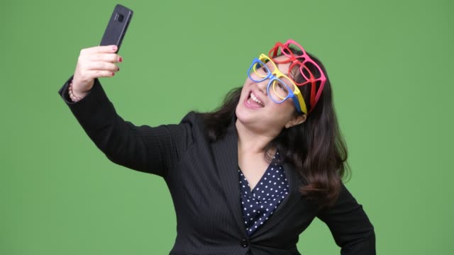 Madura-empresaria-asiática-hermosa-usar-el-teléfono-mientras-usa-muchos-lentes-como-concepto-divertido