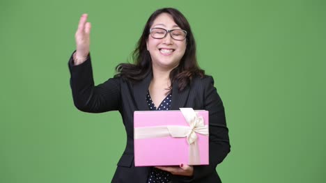Reife-schöne-asiatische-geschäftsfrau-hält-Geschenkbox-und-Daumen-aufgeben