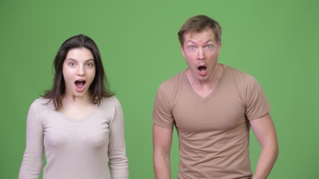 Young-couple-looking-shocked-together-against-green-background