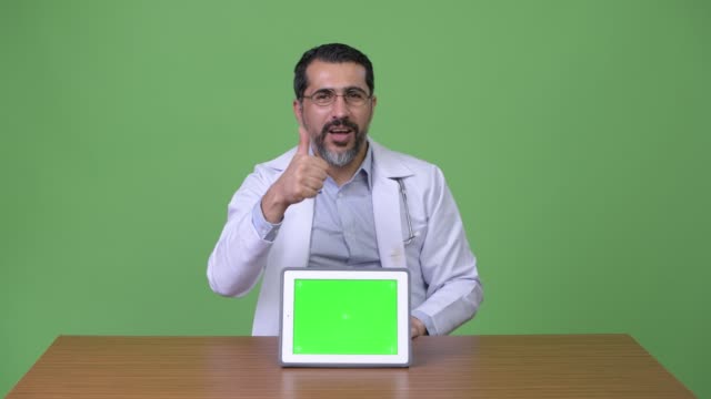 Gut-aussehend-persischen-bärtigen-Mann-Arzt-Daumen-aufgeben,-während-zeigt-digital-Tablette