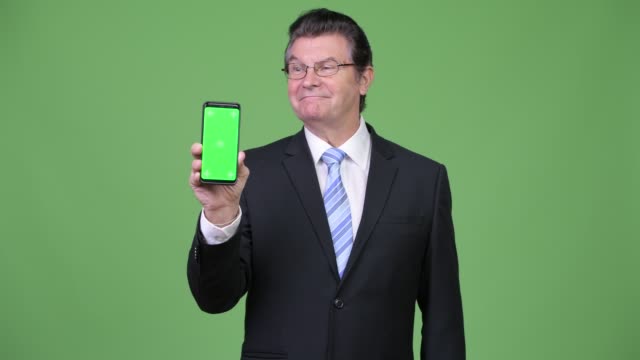 Senior-handsome-businessman-showing-phone-and-giving-thumbs-up