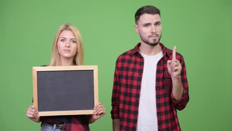 Young-couple-holding-blackboard-and-pointing-finger-up-together