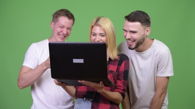 Three-happy-young-friends-smiling-while-using-laptop-together