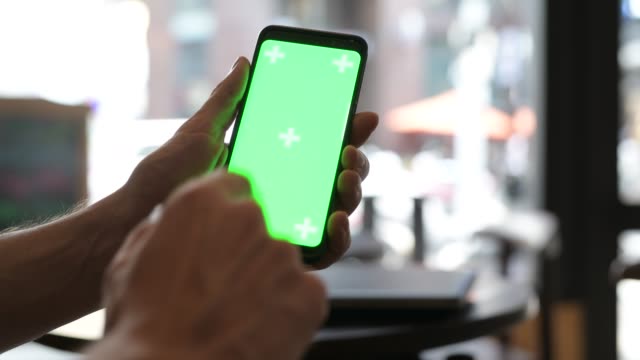 Close-Up-Of-Man-Hand-Using-Mobile-Phone-With-Green-Screen-In-Restaurant