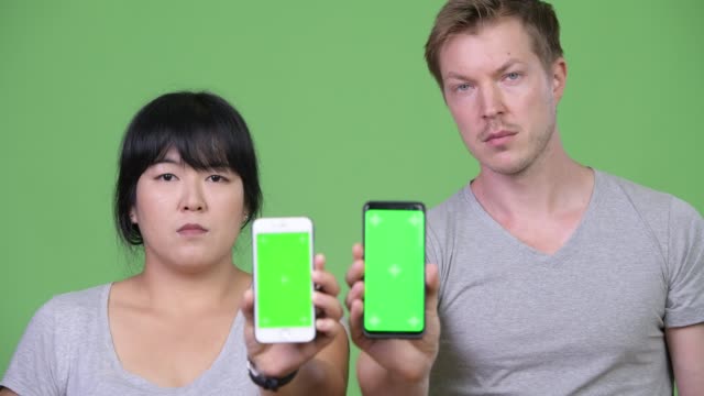 Young-happy-multi-ethnic-couple-showing-two-phones-together