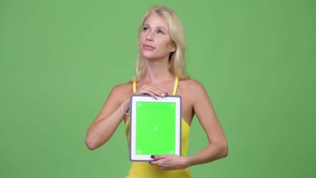 Young-happy-beautiful-blonde-woman-thinking-while-showing-digital-tablet