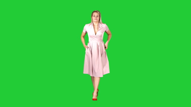 Woman-in-pink-dress-with-hands-in-pockets-is-walking-towards-the-camera-on-a-Green-Screen,-Chroma-Key