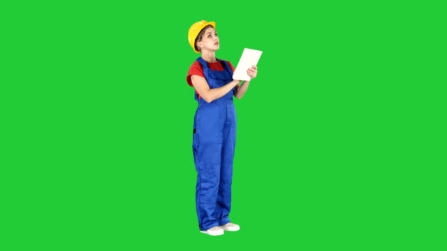 Female-engineer-in-yellow-safety-helmet-is-looking-to-tablet-computer-while-checking-for-construction-building-on-a-Green-Screen,-Chroma-Key