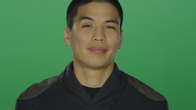 Young-man-smiles-softly,-on-a-green-screen-studio-background