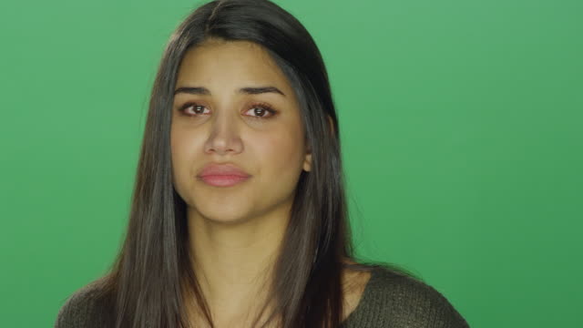 Young-woman-starting-to-cry,-on-a-green-screen-studio-background