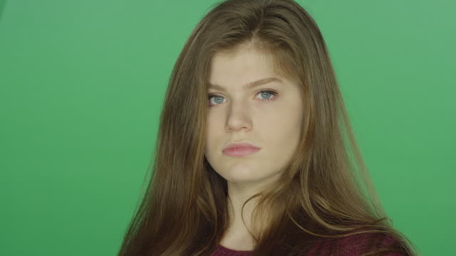 Young-brunette-woman-runs-her-fingers-through-her-hair-stares-blankly,-on-a-green-screen-studio-background