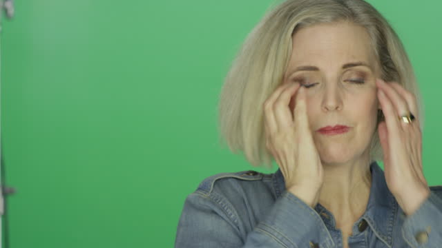 Beautiful-older-woman-suffering-a-headache-and-looking-worried,-on-a-green-screen-studio-background