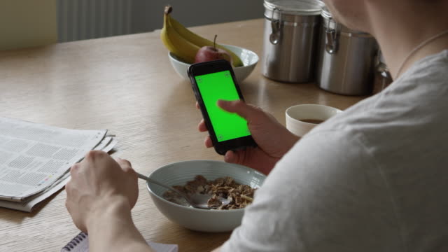 Hombre-usando-el-smartphone-con-la-pantalla-verde-y-comiendo-el-desayuno