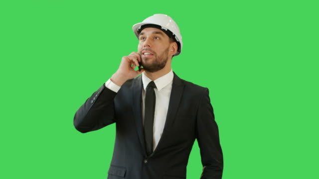 Medium-Shot-of-a-Businessman-in-a-Hard-Hat-Talking-on-the-Phone-and-Waving-Hello-to-Somebody.-Background-is-Green-Screen.