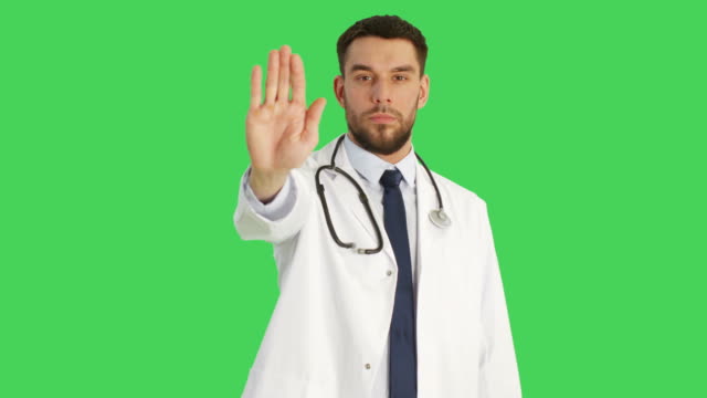 Mid-Shot-of-a-Serious-Minded-Doctor-Making-Stop-Sign-Gesture-with-His-Hand-then-Crossing-Arms-on-a-Chest.-Shot-Taking-Place-with-Green-Screen-Background.