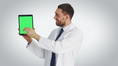 Mittelschuss-eines-Handsome-Doctor-Holding-Tablet-Computers-mit-einer-Hand-und-Making-Swiping,-Touching-Gesten-mit-einem-anderen.-Tablet-hat-grünen-Bildschirm.-Schuss-mit-weißem-Hintergrund.