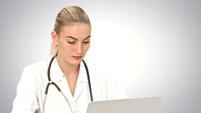 Serious-female-doctor-working-on-her-laptop-computer-on-white-background