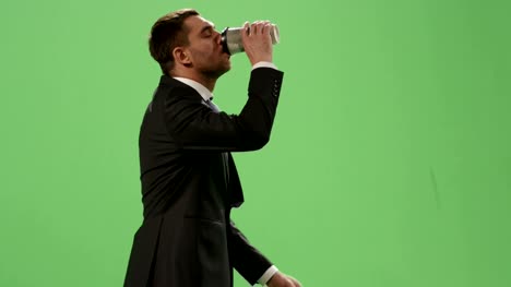 Tired-businessman-in-a-suit-is-walking-with-a-coffee-on-a-mock-up-green-screen-in-the-background.