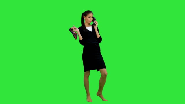 Junge-gesprächige-Frau-mit-einem-Schuh-wie-ein-Telefon-auf-ein-Green-Screen,-Chroma-Key