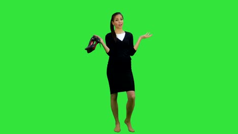Tired-young-businesswoman-standing-barefoot-and-holding-high-heels-shoes-on-a-Green-Screen,-Chroma-Key