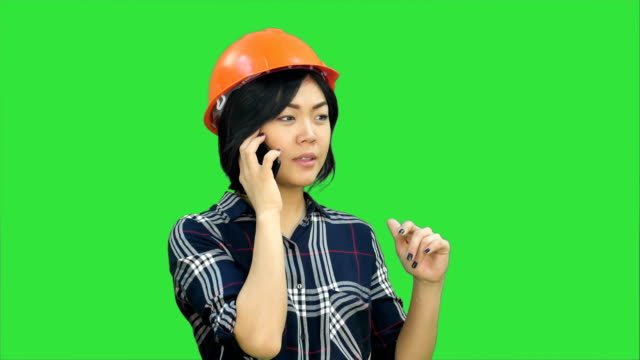 Female-engineer-with-orange-helmet-having-a-phone-call-via-smartphone-on-a-Green-Screen,-Chroma-Key