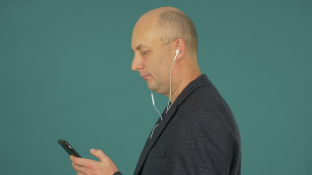 Bald-middle-aged-businessman-listening-music-with-earphones-and-smartphone