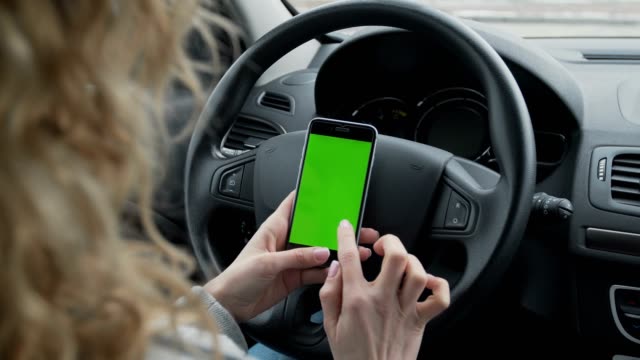 Woman-sits-in-the-modern-car-and-works-on-smartphone---closeup-hands.-Green-screen.Chroma-key