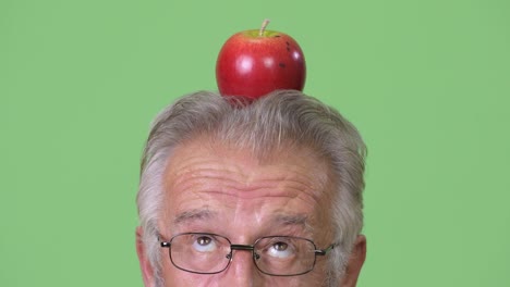 Kopf-geschossen,-der-ältere-Mann-mit-Apple-Kopfoberseite-vor-grünem-Hintergrund